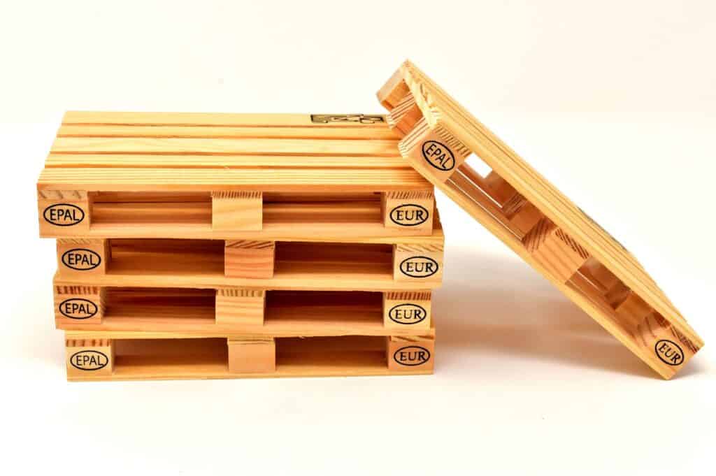 Four small wooden pallets are stacked together, with a fifth pallet leaning at an angle against the stack. Ideal for Packaging Solutions, each features EPAL and EUR markings on the sides, set against a plain white background.